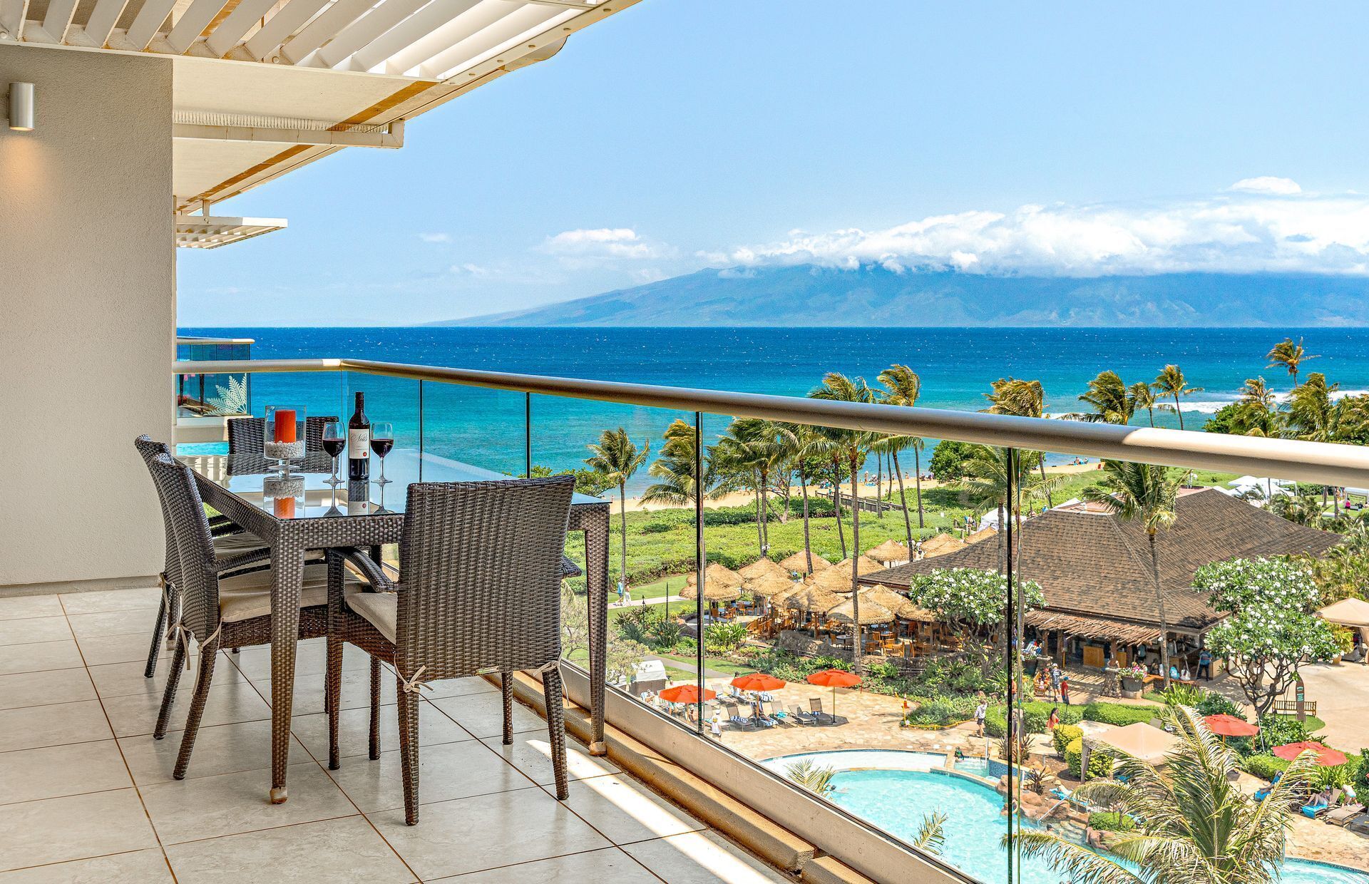 Ein Balkon mit Tisch und Stühlen mit Blick auf einen Pool und einen Strand mit Palmen.