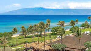 A beach resort with thatched-roof huts, palm trees, and a view of the ocean and mountains. - Maui Resort Rentals: Hokulani 605/6 –  4BR Retreat with Stunning 6th-Floor Ocean Views! (Lahaina)