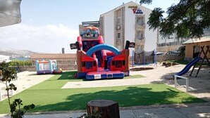 Un área de juegos al aire libre con un castillo inflable grande, un tobogán y columpios.