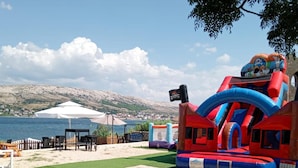 Un castillo inflable con temática pirata, una carpa blanca y vistas a un lago con colinas al fondo.