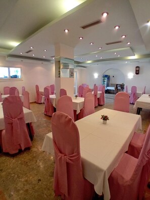 A banquet hall with multiple tables and chairs, each with a white tablecloth and pink chair covers. - Biser Hotel (Pag)