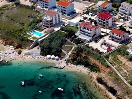 Vista aerea di una località balneare con diversi edifici, una spiaggia e acque cristalline color turchese.