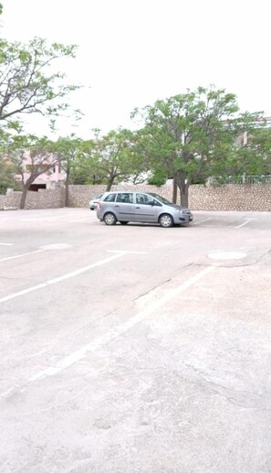 A parking area with a car, trees, and a stone wall. - Biser Hotel (Pag)