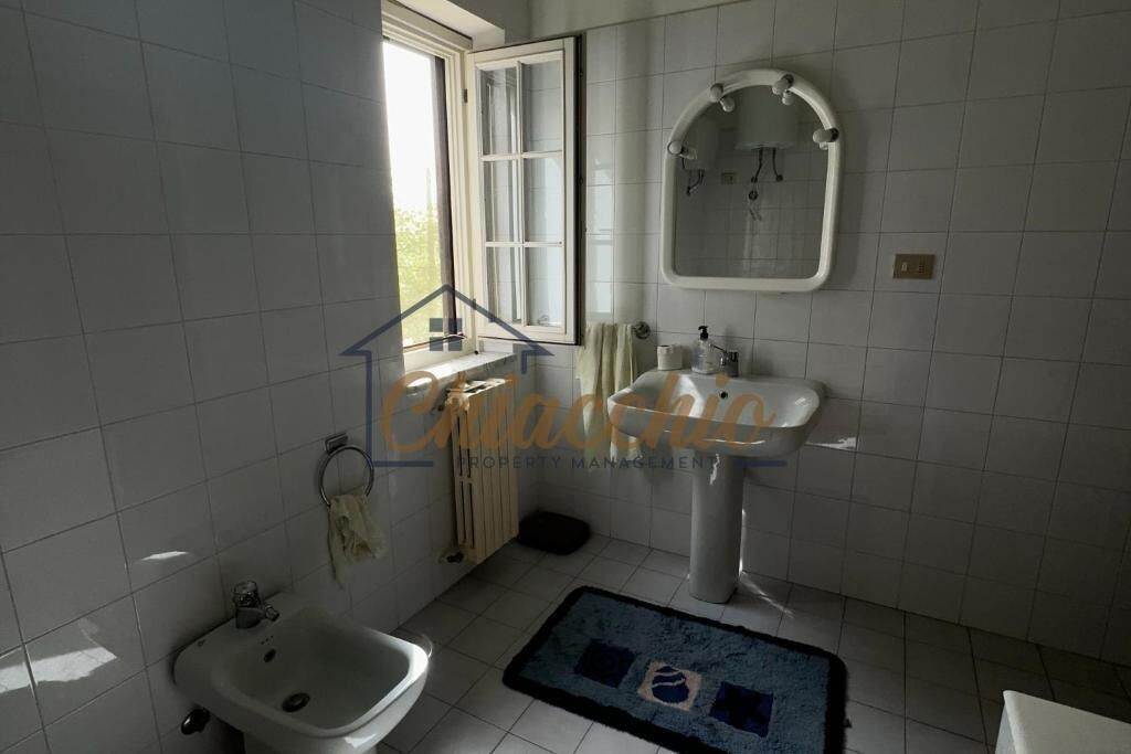 Een badkamer met een raam, een wastafel, een toiletbril en een spiegel.