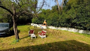 Zona verde con una maqueta de una casa, una parrilla y un coche aparcado cerca.