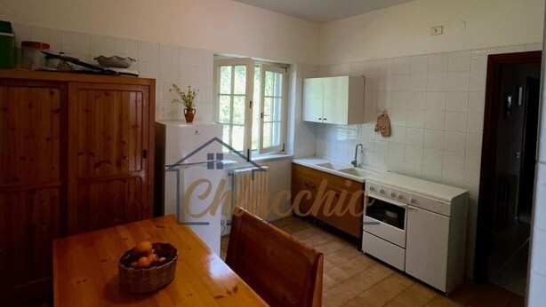Una cocina con armarios blancos, una mesa de madera con fruteros, y una ventana que proporciona luz natural.