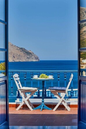 A balcony with a table and two chairs, overlooking a coastal view with a mountain and the sea. - Glaros Studios (Karpathos)
