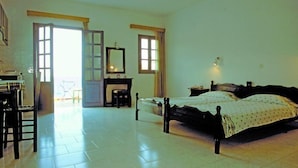 A bedroom with a bed, a dresser, a chair, and a mirror. There are two windows and a door. - Glaros Studios (Karpathos)
