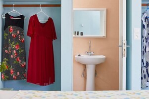 Un dormitorio con una cama, un lavabo blanco y dos vestidos colgados en una pared.