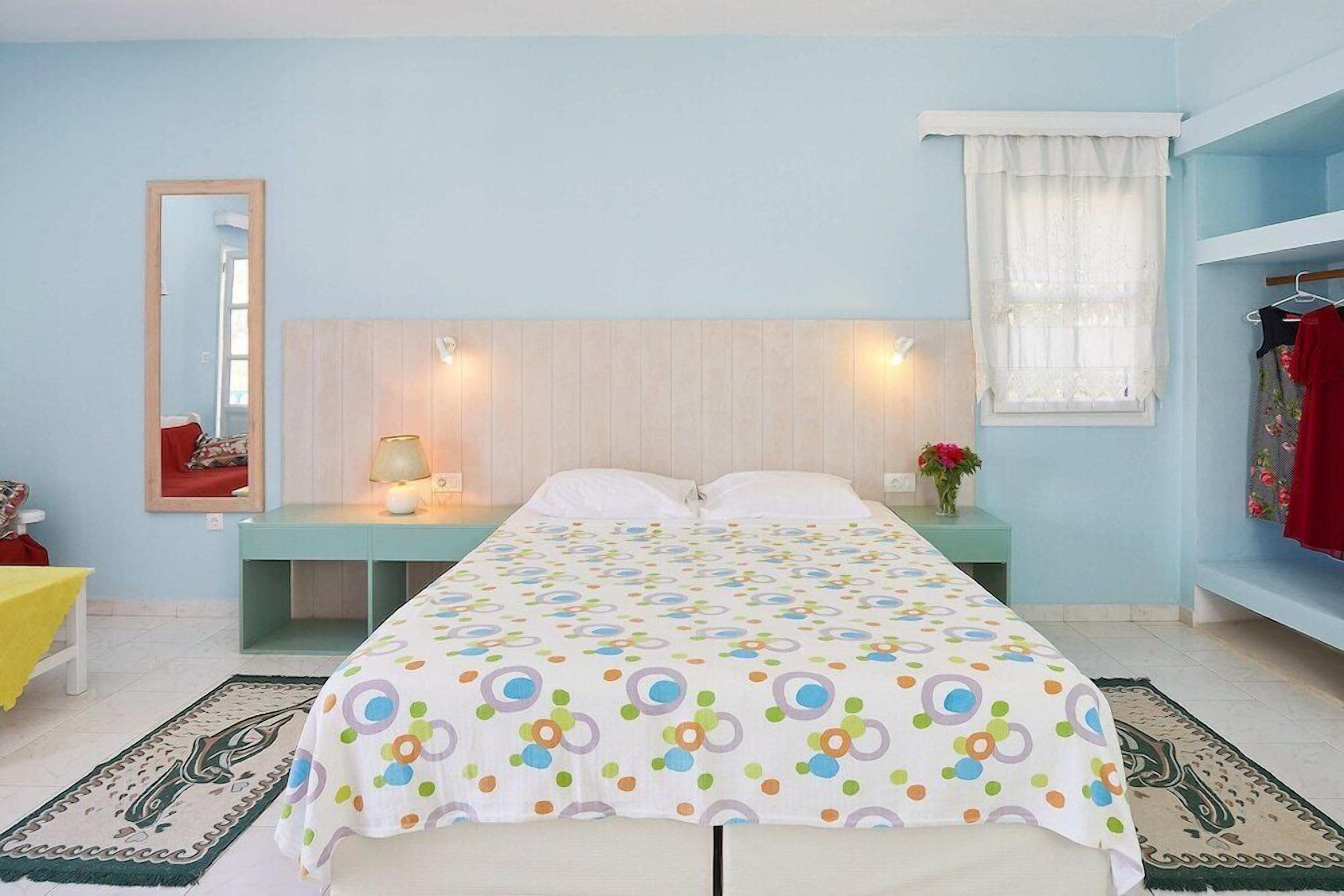 Un dormitorio con cama, mesitas de noche, espejo y ventana con cortinas.