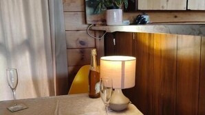 Une table à manger recouverte d’une nappe blanche, deux verres à vin, une bouteille de champagne et une lampe.