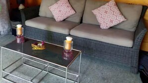 Une pièce chaleureuse avec un canapé gris, des coussins à motifs et une table basse en verre sur laquelle sont posées des bougies.