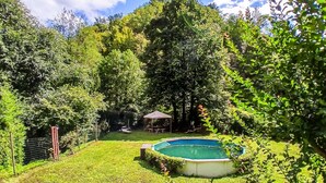 Un patio trasero con piscina, mesa de picnic y un pabellón rodeado de exuberante vegetación.