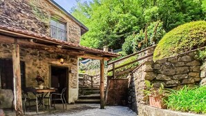 Un edificio de piedra rústico con un patio, mobiliario exterior y una pared de piedra con vegetación.