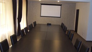 A conference room with a long table and chairs, a projector screen, and curtains. - Hotel Davos (Deva)