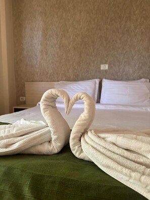 Una cama con sábanas blancas y una colcha verde, una pared con un diseño texturizado y un enchufe en la pared.