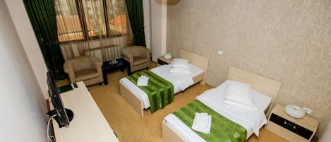 Une chambre d’hôtel avec deux lits, un bureau, une chaise, un téléphone et une fenêtre avec des rideaux.