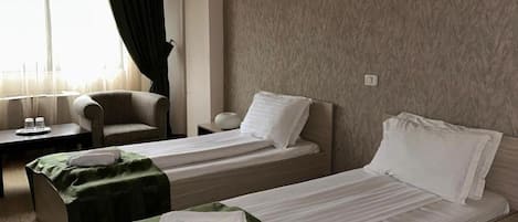 A hotel room with two beds, a desk, a chair, and a window with curtains.