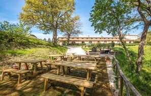 An outdoor dining area with wooden picnic tables and benches, surrounded by trees and a building with arched windows in the background. - Luxurious home in Trequanda with house a panoramic view (Trequanda)