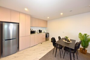 A modern kitchen with a stainless steel refrigerator, a microwave, and a stove. There is a dining table with chairs and a potted plant.