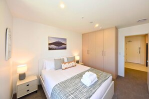 A hotel room with a bed, bedside lamps, a painting, a wardrobe, and a door leading to another room. - Fresh & Modern 1BR Stay in Manchester (Christchurch)