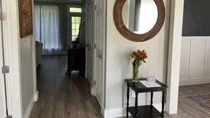 Ein Flur mit Holzboden, einem runden Spiegel an der Wand, einem kleinen Tisch mit Blumenvase und einer Tür zu einem anderen Raum.