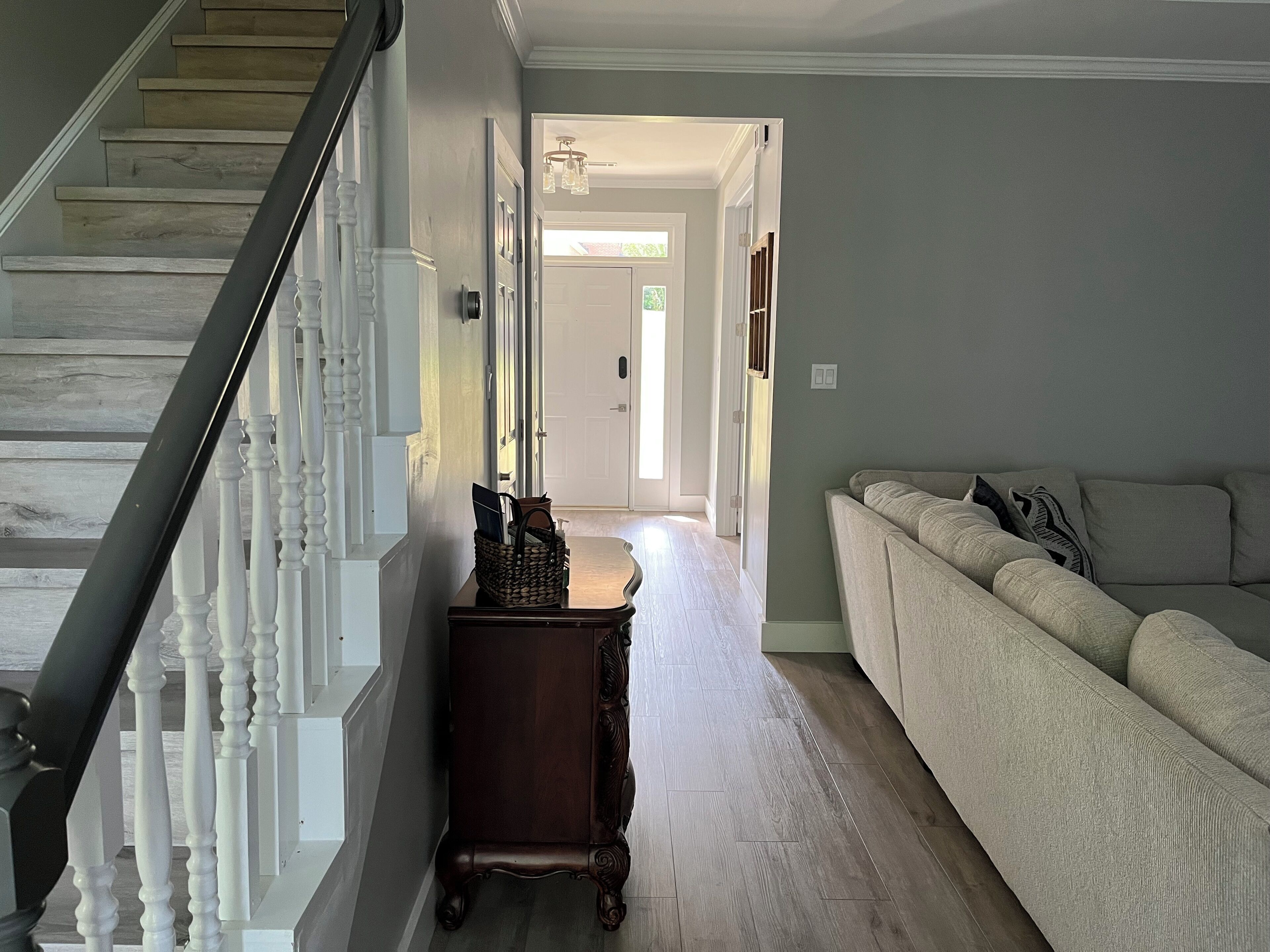 A hallway with a wooden staircase, a dark wooden side table, and a light-colored sofa.