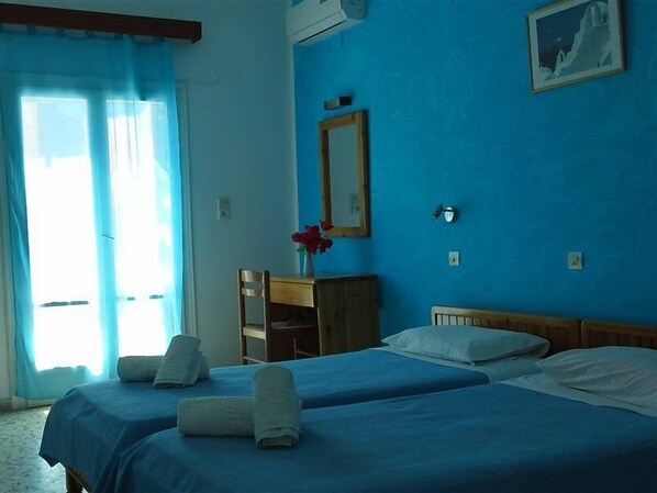 A hotel room with two beds, a wooden dresser, a vase with flowers, and a framed picture on the wall. - Dilino AND Annex Building (Santorini)