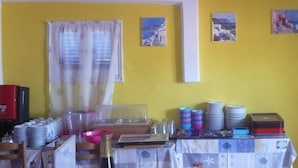 Una habitació amb una paret groga, una taula coberta amb un mantell escacat i diversos objectes com plats, gots i una ampolla.