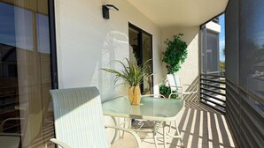 A balcony with a glass table and chairs, a potted plant, and a view of the street. - 2BR Condo at Fantasy Island – Pool, Beach , Bikes (Englewood)