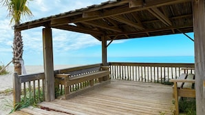 Una terraza de madera junto a la playa, con una palmera que da a la arena y al océano.