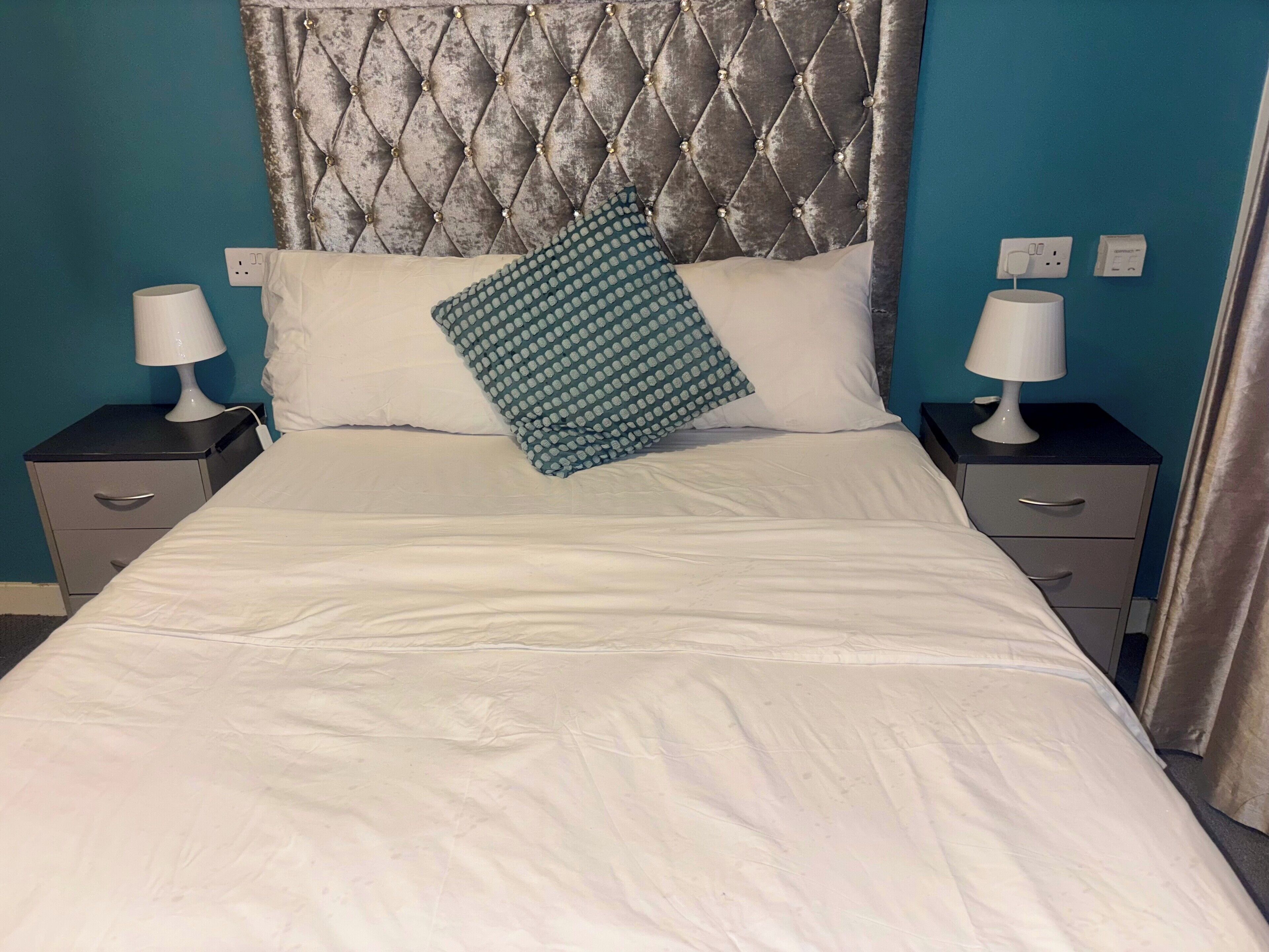 A neatly made bed with a tufted headboard, two bedside tables with lamps, and a teal accent pillow.