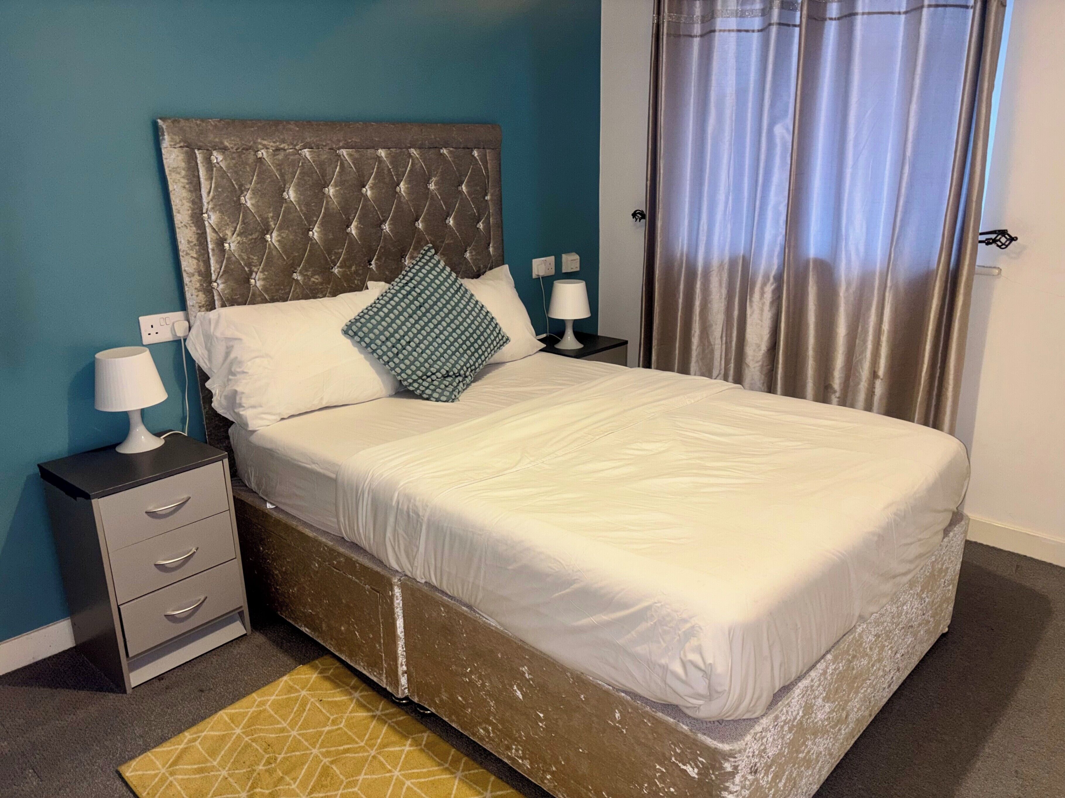 A neatly made bed with a tufted headboard, two bedside lamps, and a small drawer unit.