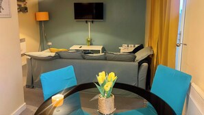 A living room with a sofa, a TV mounted on the wall, a table with chairs, and a lamp. - Peaceful Urban Retreat in Wolverhampton City (Wolverhampton)