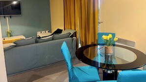 A modern living room with a sofa, a glass table with a vase of flowers, a television mounted on the wall, and a window with yellow curtains. - Peaceful Urban Retreat in Wolverhampton City (Wolverhampton)