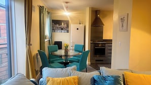 A modern living room with teal and yellow cushions, a round glass table with a vase, and a kitchen with a stainless steel range hood. - Peaceful Urban Retreat in Wolverhampton City (Wolverhampton)