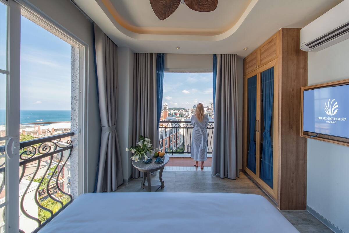 Camera d'albergo con balcone, un letto, una TV e vista sulla città.