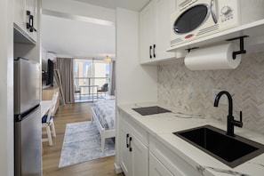A modern kitchen with a built-in microwave, a black sink, and a herringbone-patterned backsplash. - Exceptionally Clean Waikiki Studio Near Beach - Ocean & Mountain Views (Honolulu)
