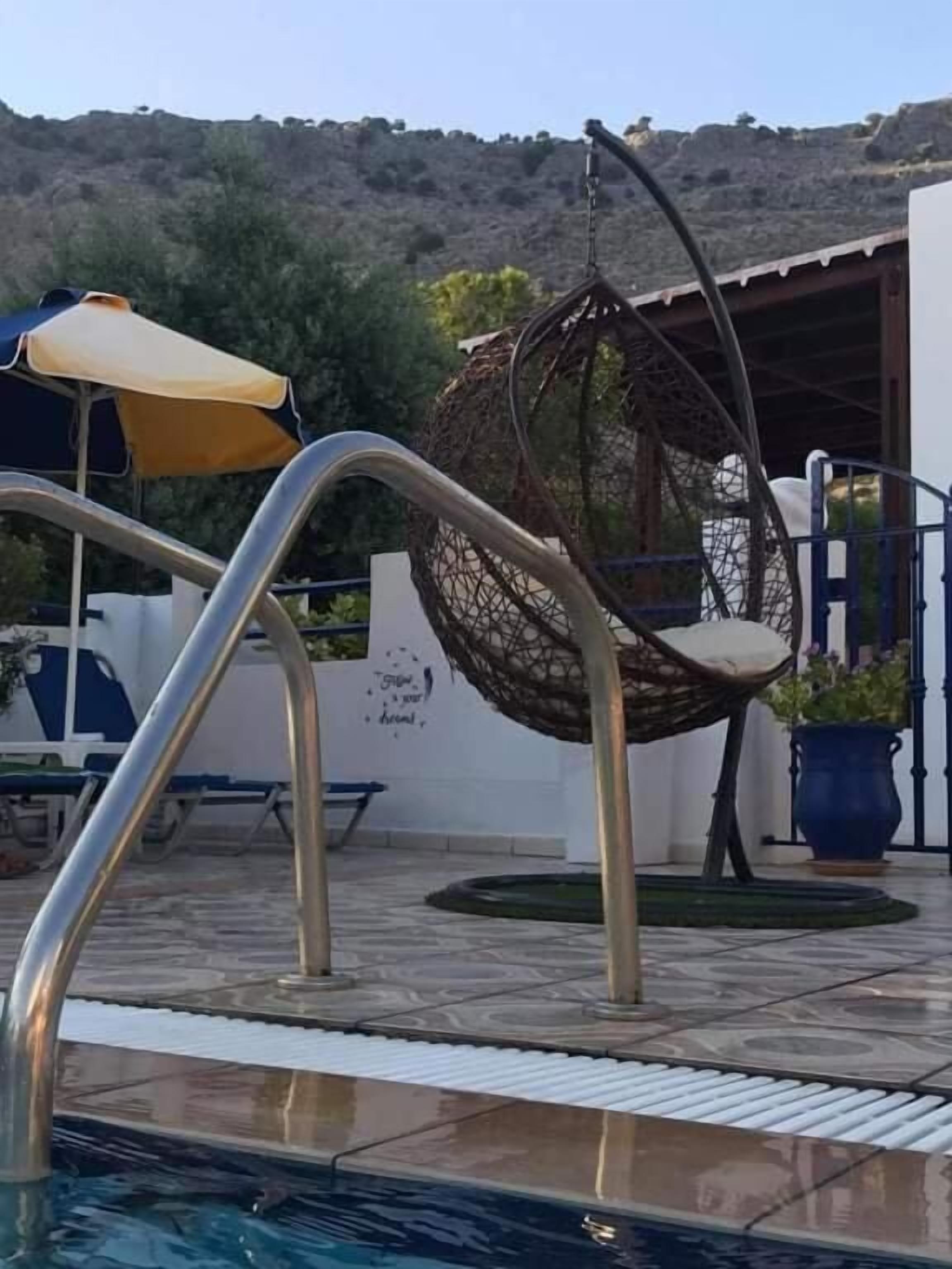 A pool area with a hanging chair, a sun umbrella, and a bench.