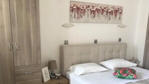 A bedroom with a bed, a nightstand, a wardrobe, and a wall-mounted artwork. - Chrysanthi Studios Apartments Pefkos (Rhodes)