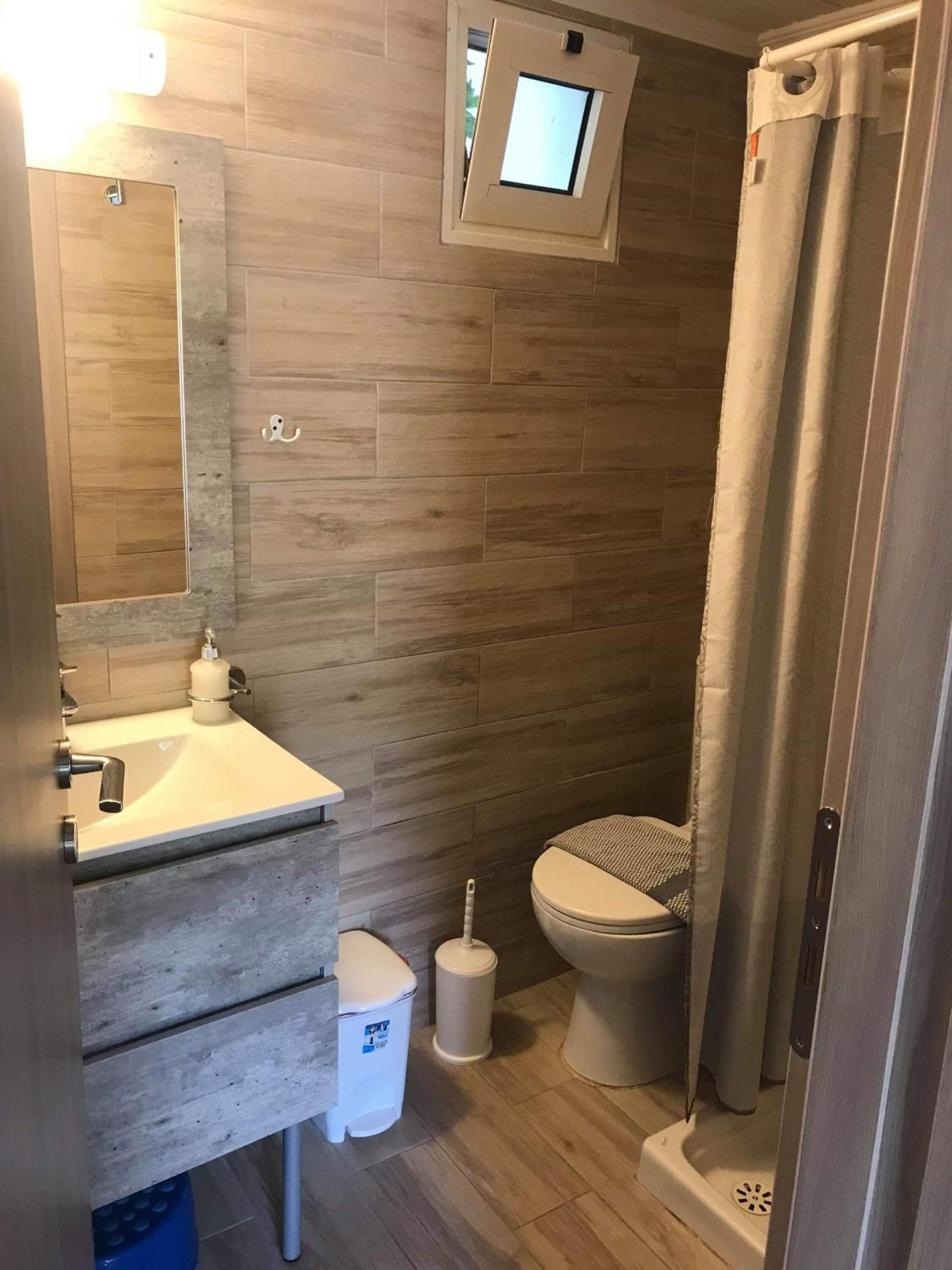 A compact bathroom with a wooden floor, a sink with a mirror, a toilet, and a shower curtain.