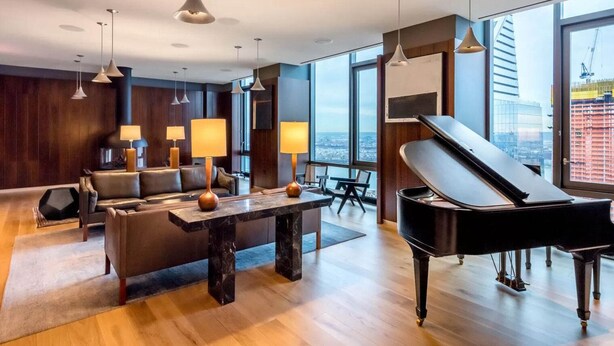 A modern living room with a grand piano, a sofa set, and a city view through large windows. - Blueground | Chelsea, rooftop, nr The Vessel (New York)