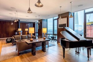 Uma sala de estar moderna com um piano de cauda, um conjunto de sofás e vista para a cidade através de grandes janelas.