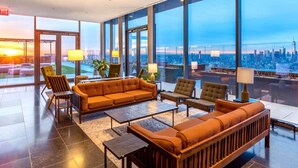 A spacious lounge area with a large sofa, armchairs, and a coffee table, featuring large windows with a city view. - Blueground | Chelsea, rooftop, nr The Vessel (New York)