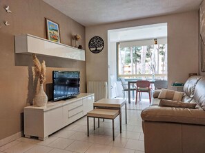 Ein Wohnzimmer mit Fernseher, Sofa und Esstisch.
