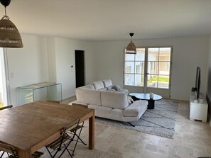 A living room with a sofa, a coffee table, a dining table, and a TV. - New house on the Ile de Re at the edge of the ocean with breathtaking views! (Rivedoux-Plage)
