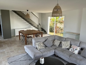 A modern living room with a grey sectional sofa, a dining table, and a staircase. - New house on the Ile de Re at the edge of the ocean with breathtaking views! (Rivedoux-Plage)