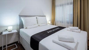 A hotel room with a neatly made bed, a bedside table with a lamp, and a window with curtains. - 1 BR City Apartment Adialuxe S5, Rijeka, Croatia (Rijeka)