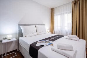 A hotel room with a neatly made bed, a bedside table with a lamp, and a window with curtains. - 1 BR City Apartment Adialuxe S5, Rijeka, Croatia (Rijeka)
