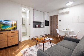 A modern living room with a sofa, a coffee table with a magazine, and a TV displaying a scenic landscape. - 1 BR City Apartment Adialuxe S5, Rijeka, Croatia (Rijeka)